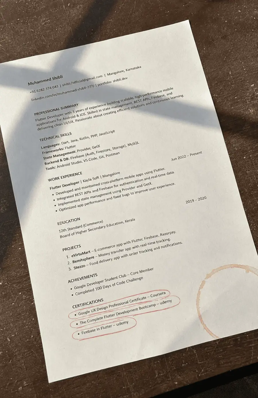 A printed resume on a desk with certifications circled in red pen.